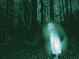 A grainy image shows a white ghostly figure standing in a dark woodland.