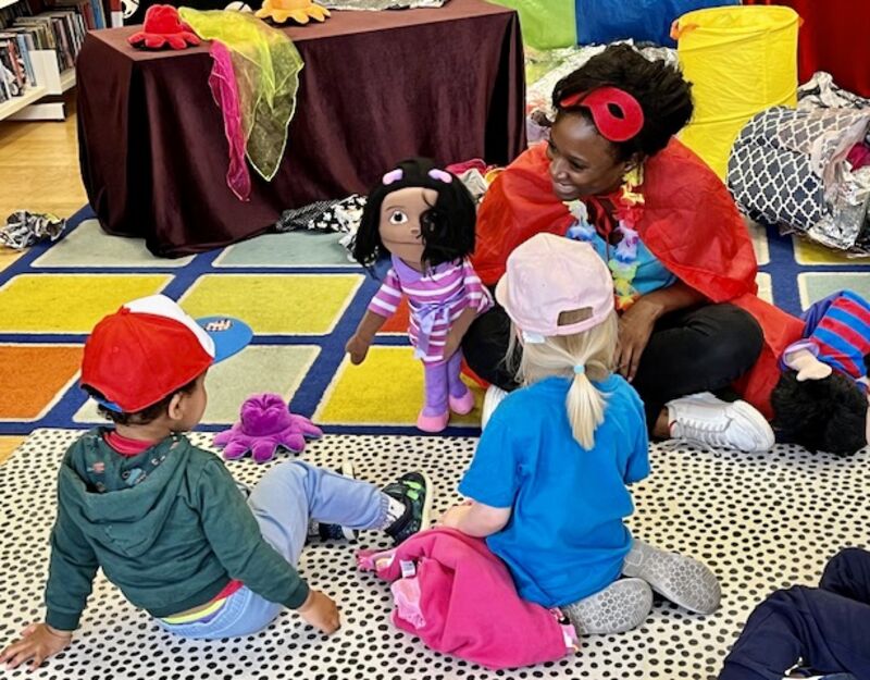Woman holding up puppet to young boy and girl who are talking with the puppet.