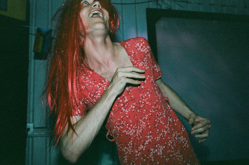 An artist performing in a red wig and a red dress