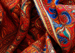 Close-up of a richly patterned red saree fabric with folds, showing detailed blue, teal, orange and cream motifs inspired by traditional textile design.