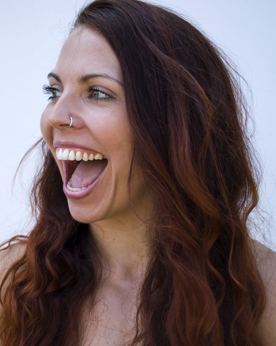 A woman with reddish-brown hair, looks to the side, open-mouthed in delight/laughter.