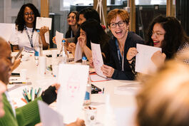 Photo is of happy smiling people sitting around a table holding up images they have drawn