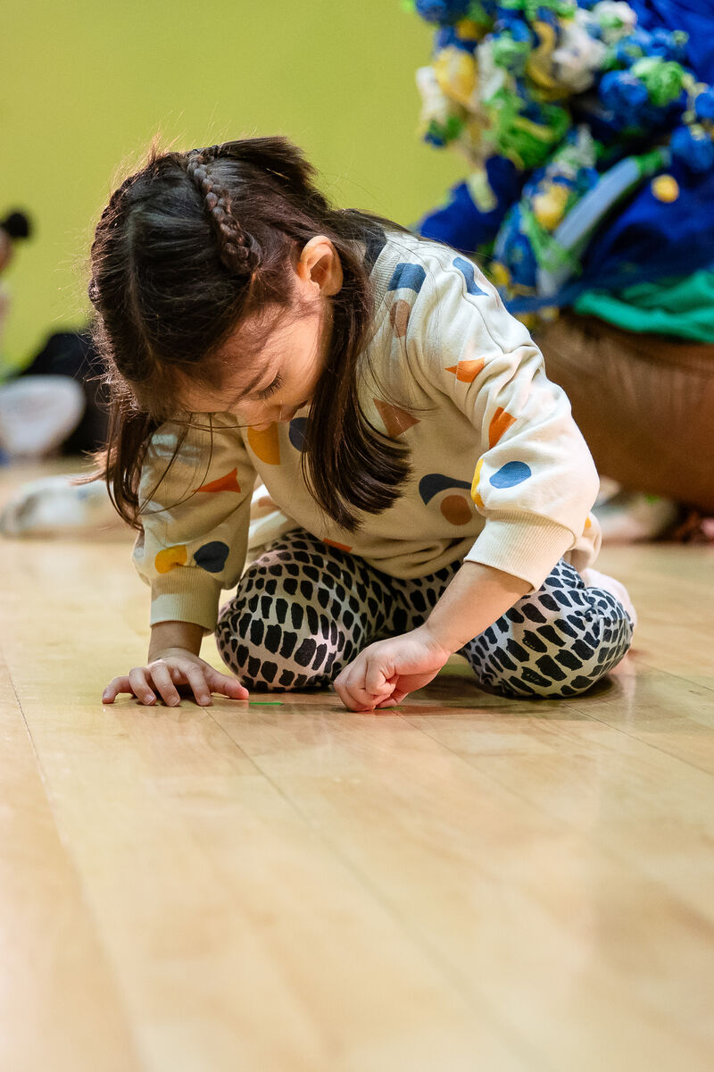 A young girl is playing with tape, sticking it to a wooden floor 