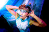 South East Asian woman in blue make up and costume looking into distance with hands behind head