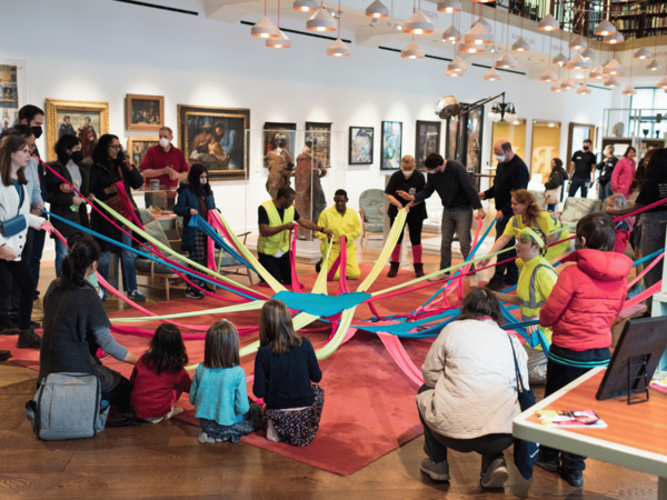 A group of people, including BLINK facilitators wearing high-vis tops, are dancing with an octoband; a brightly-coloured lycra circle with long arms coming off that everyone can hold on to  