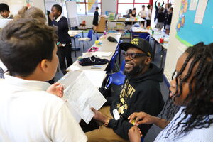 Man in cap and hoodie smiling, looking at a poem, while two children gather around him