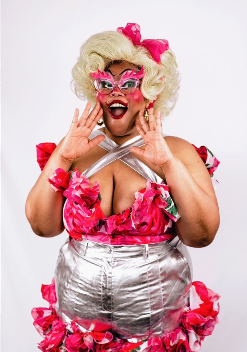 Nat Funni dressed in a silver an pink outfit and a pink mask against a white background