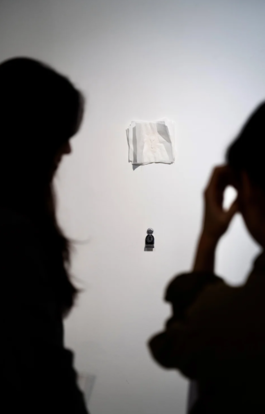 Image of a cast object presented on a wall. Figures in the foreground take a photo of it