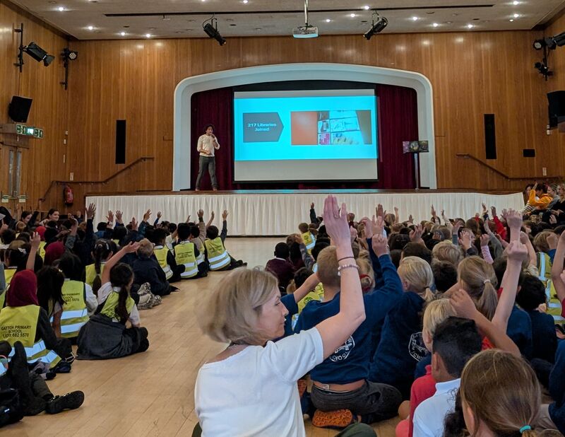 Children sitting in hall watching Joseph Coelho presenting on stage