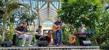 A band plays instruments amongst plans in a large greenhouse