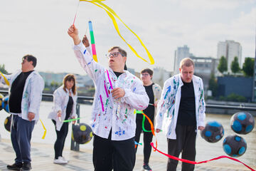 a group of people wearing white shirts with paint splatters on hold brightly coloured ribbons