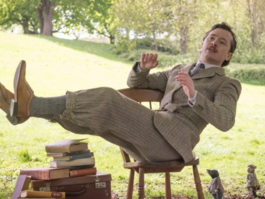 white man in grey suit, leaning on wooden chair in park