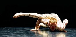 A person in a leotard patterned in flowers crouches and looks forward into the audience