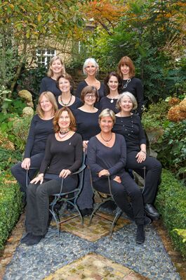 A group of women wearing black pose together in a garden