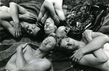 Black and white photograph of four white men lying down with their arms crossed on their chests, eyes closed