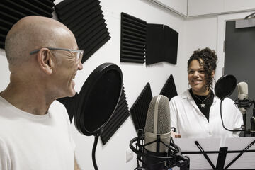 Two Actors Stand Behind Microphones Recording