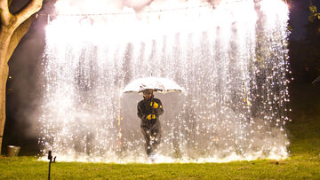 Outdoors, a man holds up an umbrella as brightly glowing stuff rains from the sky.