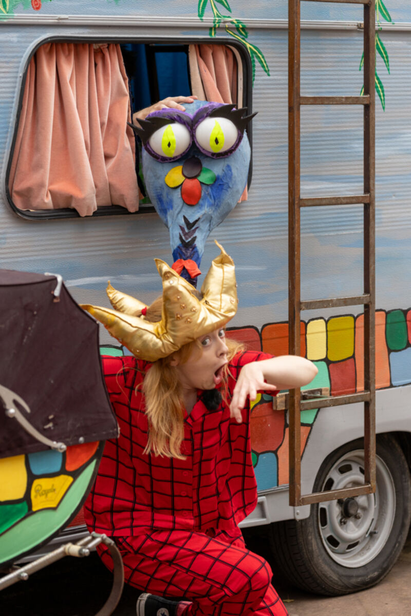 A dragon's head pops out of a caravan window.  A queen crouches beneath the window.