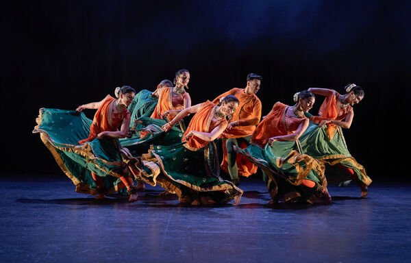 6 South Asian dancers in orange and green costume dance onstage