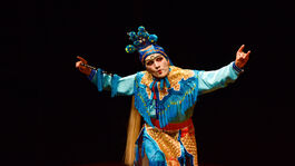 A man wearing an intricate blue and gold costume poses with his arms out and curved up.