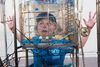 White woman with blonde hair, wearing blue t-shirt and cap, looking through glass marble run filled with water, so her face is warped 