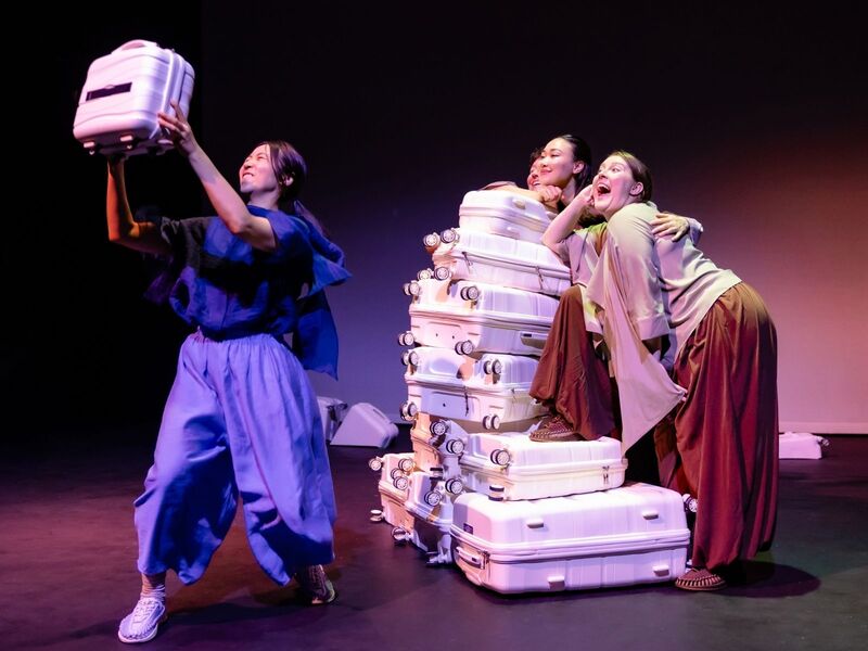 Production shots from Transit - the first is a group of actors crowded around a tower of suitcases while one pretends to take a selfie using a smaller suitcase; the second is a group of actors standing behind a row of suitcases with projections describing how much they've spent on migrating to the UK; the third is a group of actors clumped together in low light, their arms stretched out to the ceiling mid-contemporary dance; the fourth is an actor standing in between two harsh lights with words projected over her face; the fifth is five actors standing in the corners and centre of the stage, 'talking' to the home office via mimed phones.