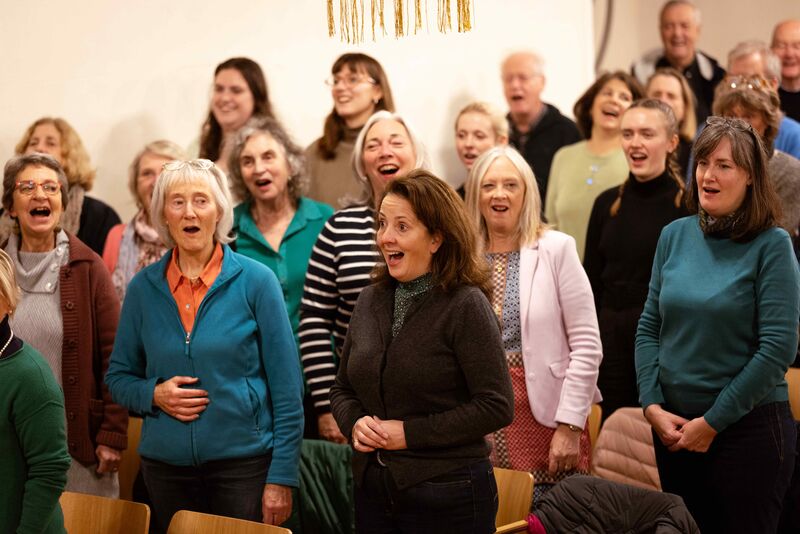The picture shows some singers doing a singing warm-up exercise and smiling