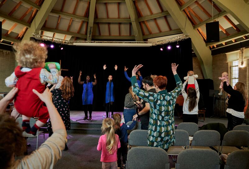 gospel choir performing on stage in background, audience members on their feet with hands and babies in the air.
