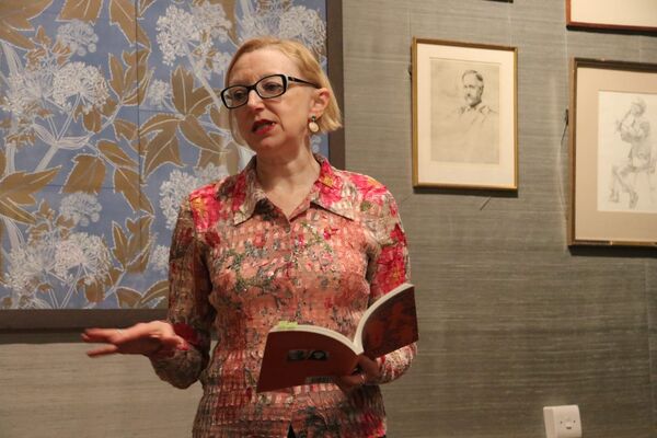 Hilaire standing a literary event, holding a book open in her left hand, looking to her left and speaking.