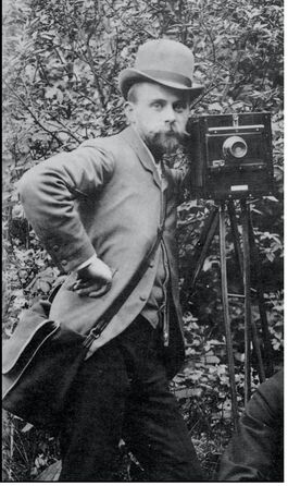 Image of Paul Martin posing alongside camera.  He has a beard and moustache and is wearing a jacket with his hand on his hip
