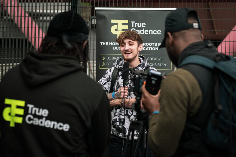 Young person being interviewed in front of a sign for community organisation True Cadence