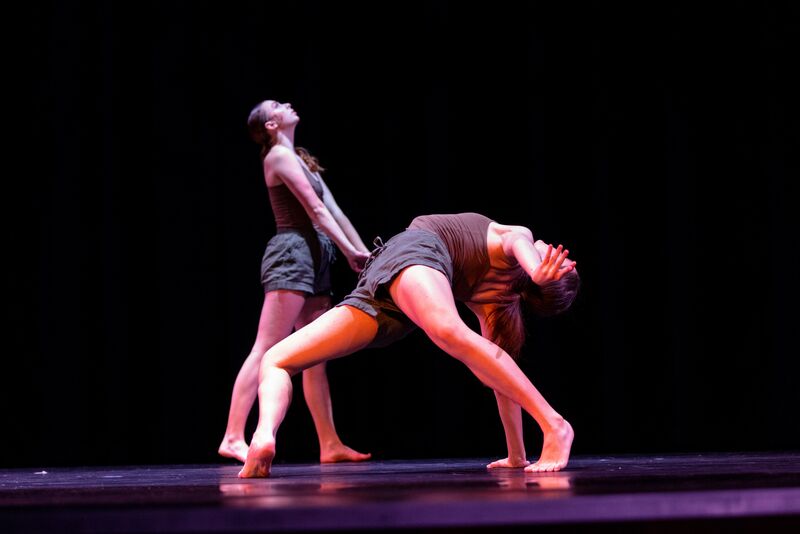One dancer arches backward on the floor, while a second dancer stands behind her, looking up and to the side. 
