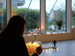 A woman paints a round mandala canvas in an warm intimate candle lit large window yoga studio