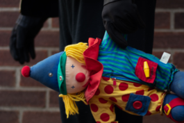 A black gloved hand holding a toy of a clown on its side