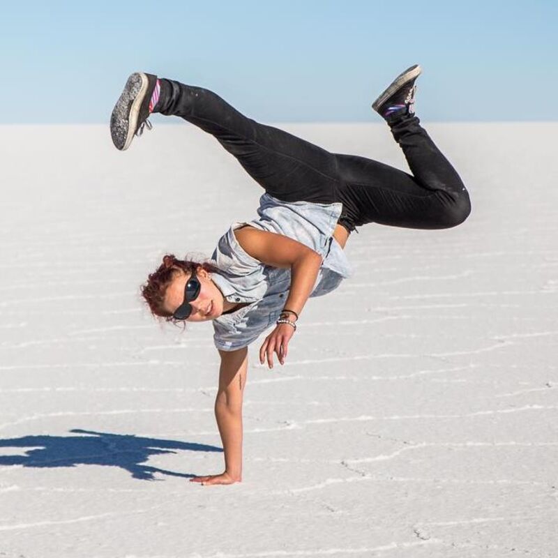 A woman, balances on one-hand doing an 'L-kick', on salt flats.