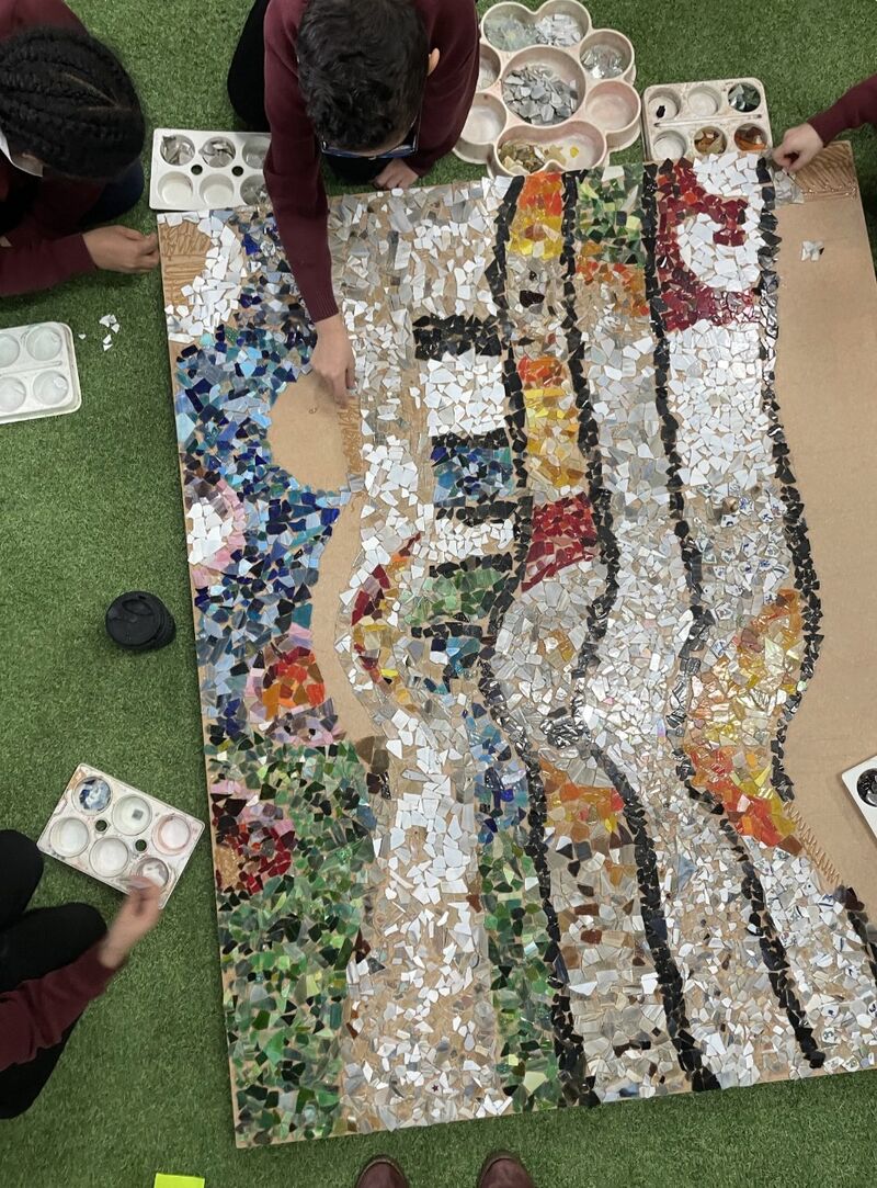 Children's hands adding mosaic pieces to a big panel inspired by Antoni Gaudí at Chesterton School.