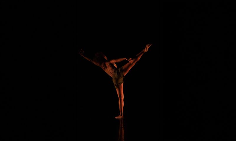 A dancer kicks one leg up to the side, facing away from the camera. 