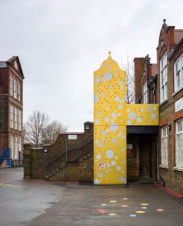 A converted Victorian school building with a golden lift covered in silver bubbles on the outside.