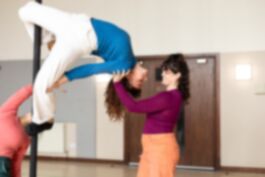 Two women climb a pole, facing each other. They each have one foot on the pole with their other leg extended away in the air. They are 2m from the floor.