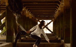 Woman dances under Pier along the River Thames, wearing white shirt and black trousers with hair and clothes wet.