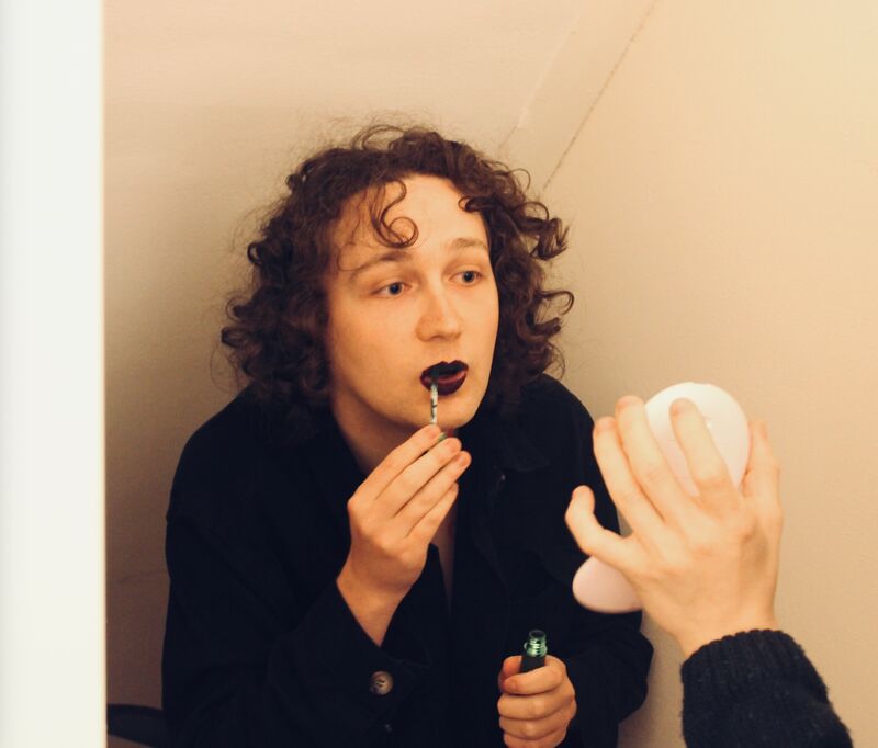 an artist applying black lipstick while a participants holds up a small mirror