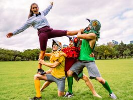 Three performers dressed as pigeons lift a young woman in business clothing.
