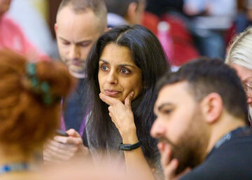 a close up photo of an Asian woman with black hair and a white man with brown hair looking intensely at something with their hands under their chins