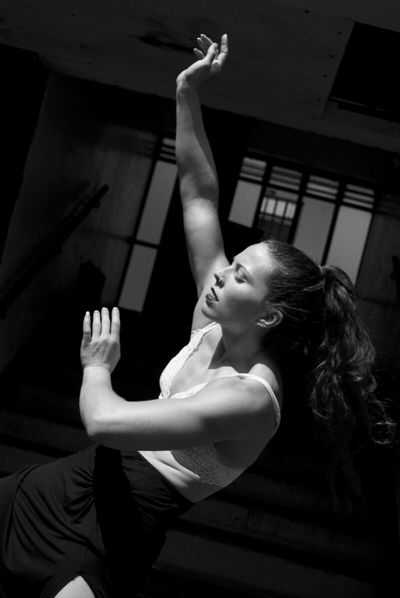 A woman dances, with her back curved, one arm reaching up to the sky and the other bent in front of her.