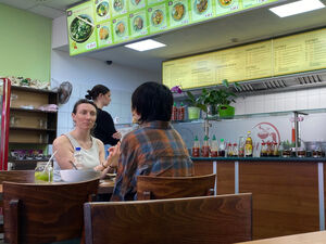 Interior of a cafe. There are people seated at a table facing each other engaged in conversation with the remains of their lunch on the table.