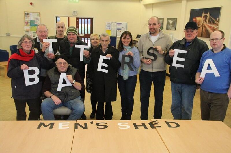 Images shows a group of people each holds a letter cut out of paper and together it reads 'Battersea Men's Shed'