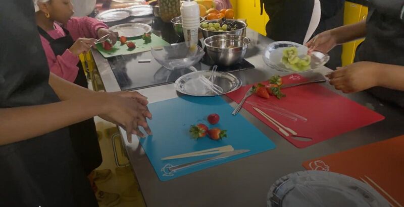 Children stand around a stainless steel chefs island, chopping strawberries on colourful chopping boards. There is a whole array of other fruit to choose from. Kitchen safety and knife skills assessment and teaching in motion. Exotic fruit kebabs were the the dish of the day, with optional chocolate dipping sauce. And yes, a vegan chocolate alternative was available to suit all dietary needs.